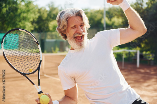 Celebrating victory. Senior modern stylish man with racket outdoors on tennis court at daytime © standret