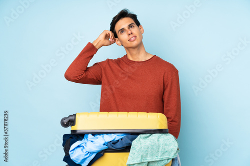 Man with a suitcase full of clothes over isolated blue background having doubts and with confuse face expression photo