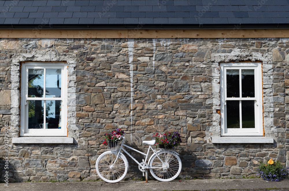 White painted decorative bicycle with flowers against stone wall house in rural Ireland
