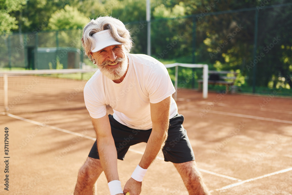 Playing game. Senior modern stylish man with racket outdoors on tennis court at daytime