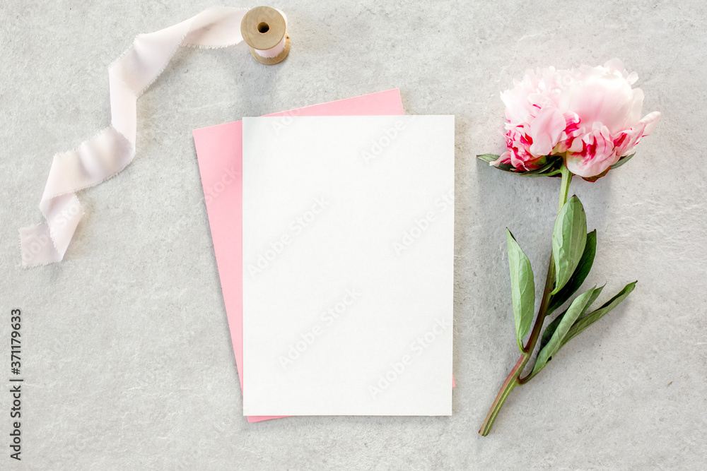 Mockup invitation, blank paper greeting card, pink envelope and peonies on gray stone table. Flower background. Flat lay, top view. Mockup invitation, blank paper greeting card, pink envelope and peonies on gray stone table. Flower background. Flat lay, top view.