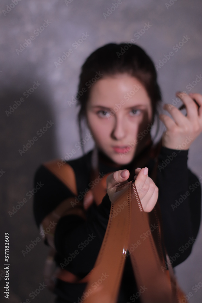 brunette girl in a black turtleneck wrapped in a film reel on a gray wall background