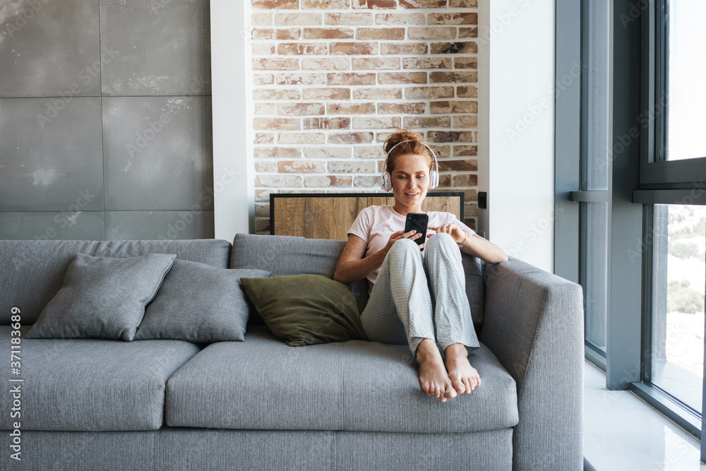 Image of woman using headphones and cellphone while sitting on couch Image of woman using headphones and cellphone while sitting on couch