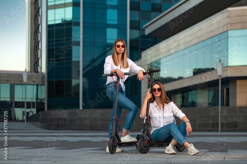 Beautiful young women is enjoying sunny summer day while riding around the city on electro kick scooters. Lifestyle.
