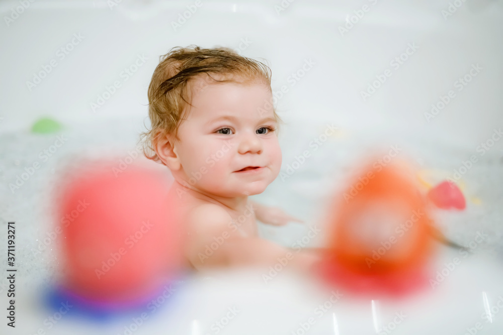 Cute adorable baby girl taking foamy bath in bathtub. Toddler playing with bath rubber toys. Beautiful child having fun with colorful gum toys and foam bubbles Cute adorable baby girl taking foamy bath in bathtub. Toddler playing with bath rubber toys. Beautiful child having fun with colorful gum toys and foam bubbles