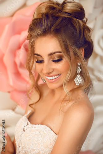 Attractive young bride with makeup and fashion wedding hairstyle. Closeup portrait of young gorgeous woman over roses wall flowers. Studio shot.