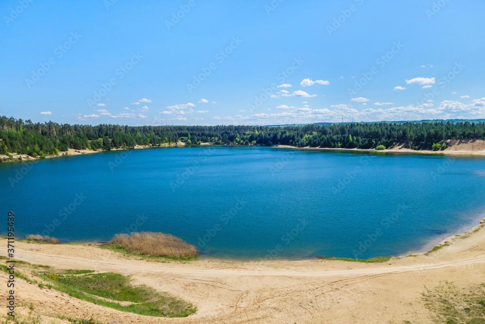 Dark blue lake surrounded by pine forest. Lake arose on site of former industrial quarry
