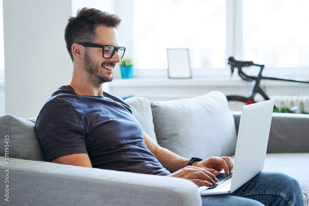 Satisfied man sitting on couch using laptop working from home Satisfied man sitting on couch using laptop working from home