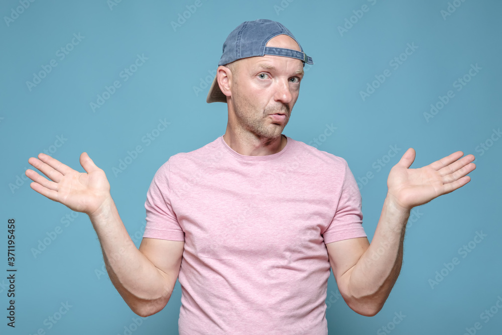 Man with an innocent expression on face spreads arms to the sides and looks at the camera in bewilderment. Blue background. Man with an innocent expression on face spreads arms to the sides and looks at the camera in bewilderment. Blue background.