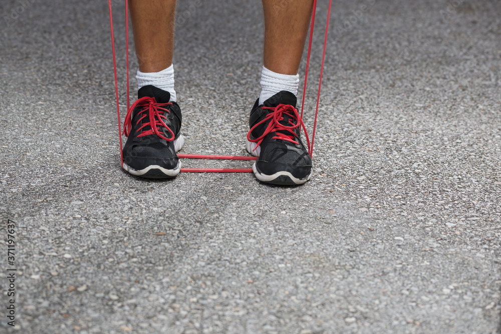 A man working out outdoors using red elastic band.