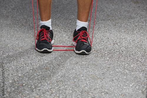 A man working out outdoors using red elastic band.