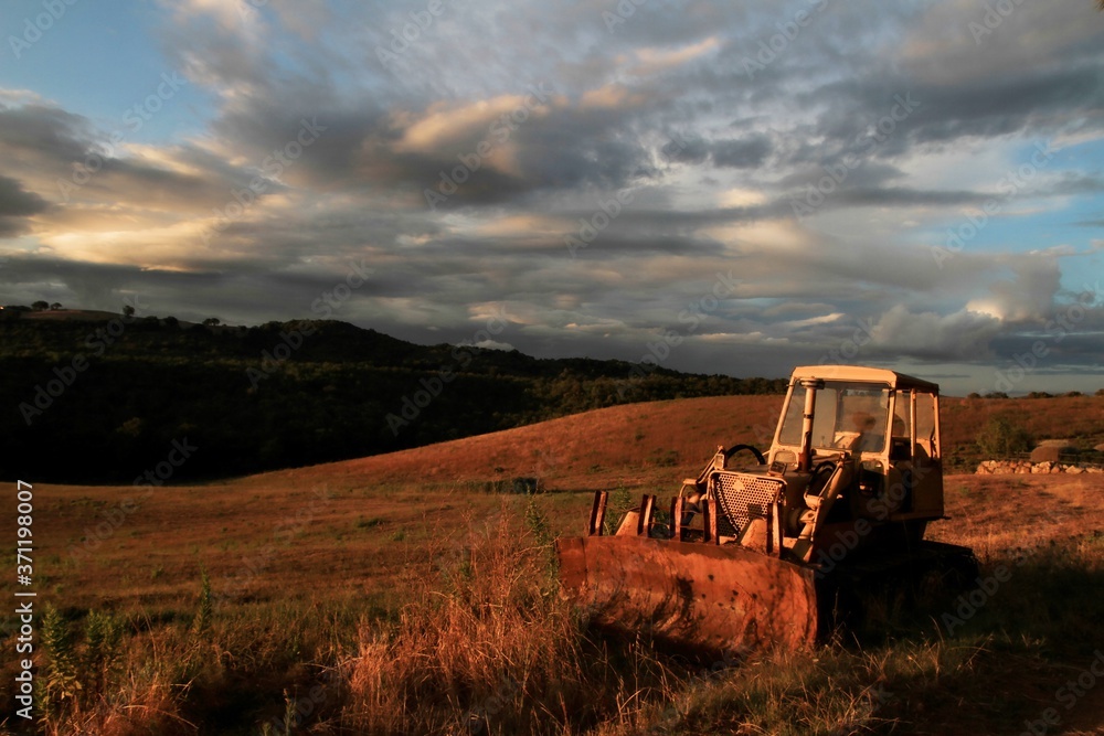 Fototapeta premium Sunset on the Tuscan Maremma. Old agricultural machine in the foreground.