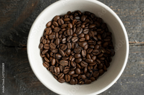 Bowl filled of fresh arabica or robusta coffee beans on a wooden table.