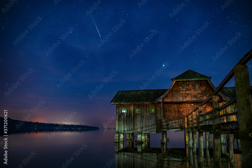 Sternschnuppe über einem Bootshaus am See in Bayern 