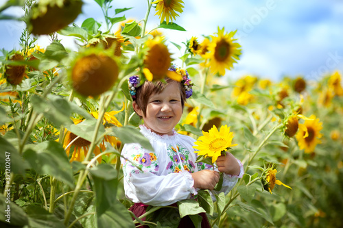 
Happy smiling Ukrainian girl in an embroidered shirt and a wreath of flowers with a yellow and blue flag in her hands on a field of sunflowers. Ukraine's Independence Day. National flag day