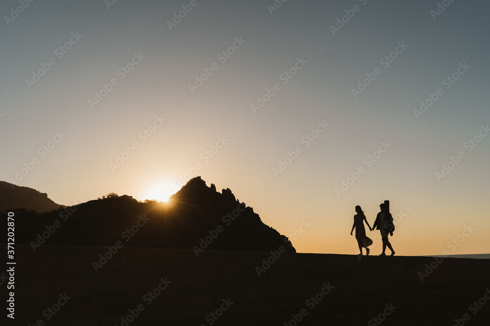 Silhouettes of a couple in love. Romantic photography near the mountains. A young couple is walking by the sea. Lovestori newlyweds