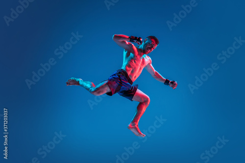 High flight. MMA. Professional fighter punching or boxing isolated on blue studio background in neon. Fit muscular caucasian athlete or boxer fighting. Sport, competition and human emotions, ad.