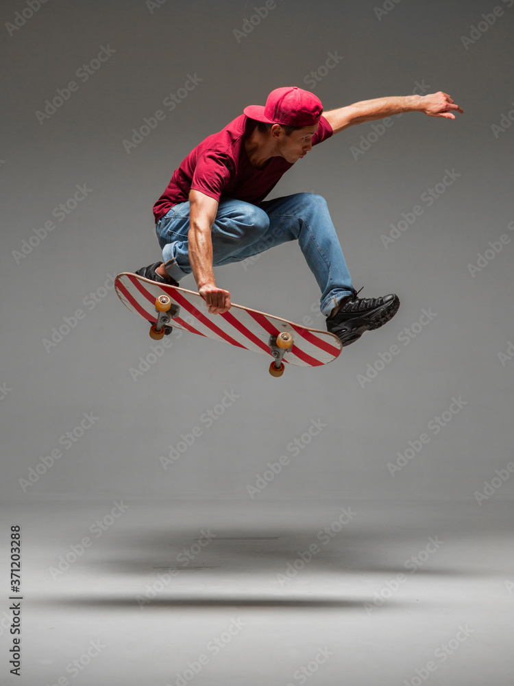 Cool guy skateboarder jumps on skateboard in studio on grey Photography about skateboarding tricks Stock Photo | Adobe Stock