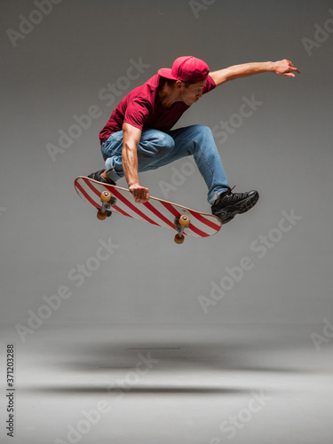 Cool young guy skateboarder jumps on skateboard in studio on grey background. Photography about skateboarding tricks photo