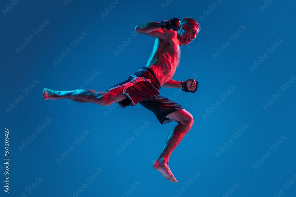 High flight. MMA. Professional fighter punching or boxing isolated on blue studio background in neon. Fit muscular caucasian athlete or boxer fighting. Sport, competition and human emotions, ad.