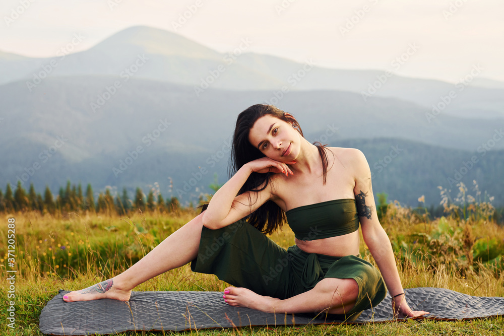 Cute brunette sits on yoga mat. Majestic Carpathian Mountains. Beautiful landscape of untouched nature Cute brunette sits on yoga mat. Majestic Carpathian Mountains. Beautiful landscape of untouched nature