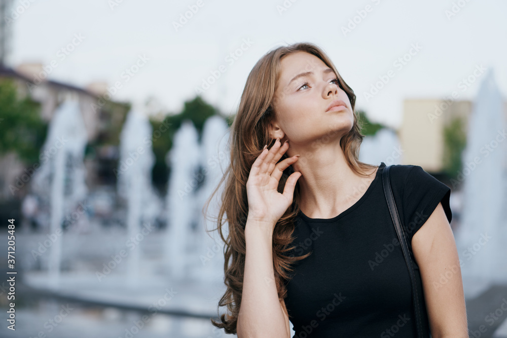 Woman near the fountain in the street in a black T-shirt cropped view of her loose hair beautiful model face Woman near the fountain in the street in a black T-shirt cropped view of her loose hair beautiful model face
