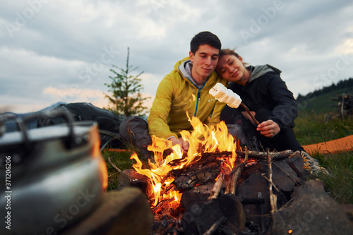 Couple with marshmallow near campfire. Majestic Carpathian Mountains. Beautiful landscape of untouched nature