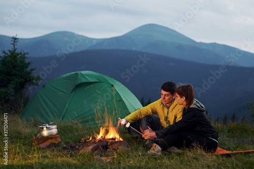 Classical marshmallow making near campfire. Young couple. Majestic Carpathian Mountains. Beautiful landscape of untouched nature