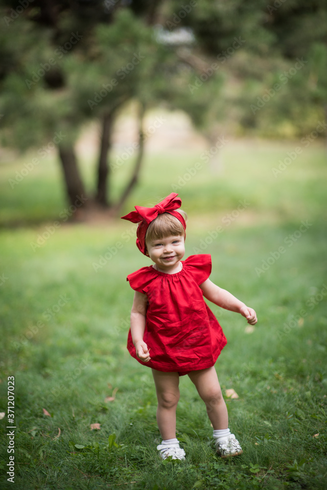 small blond girl in red dress smile and stay on green grass small blond girl in red dress smile and stay on green grass