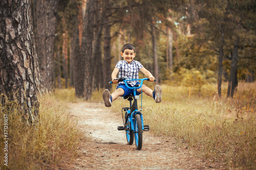 Funny boy cyclist rides in the sunny forest on a bike. Adventure travel.