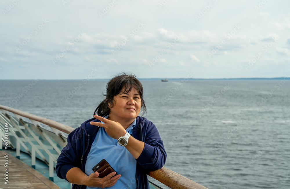 Photo of an Asian woman in her 50s makes a v-sign. Blue ocean and sky background