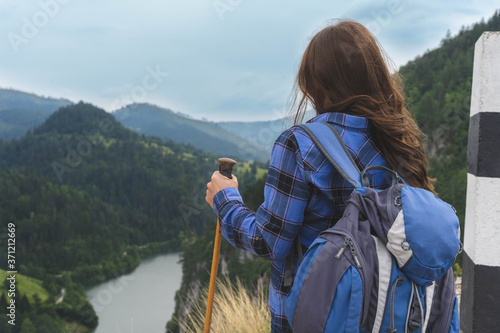 Rear view of hiker woman on mountain top. She is looking on lake. Wearing big backpack and climbing sticks. Tara national park concept 