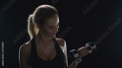 Fitness woman lifting weight dumbbell and looking to camera on black background