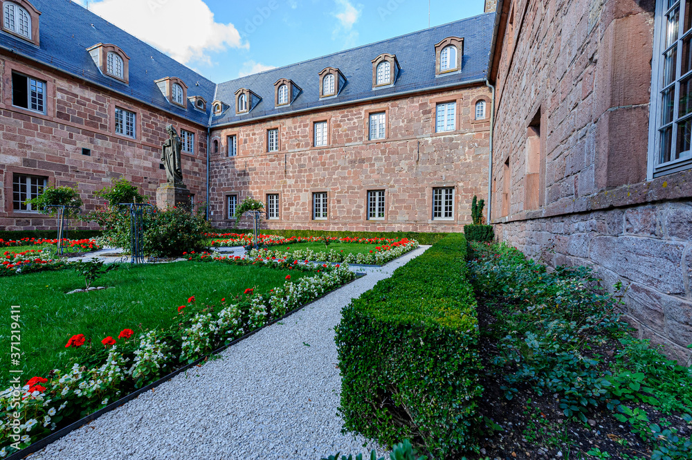 The cloister of the monastery of Saint Odile in Alsace. The buildings are made of pink stones from the region. Beautiful flowerbeds and gravel paths.