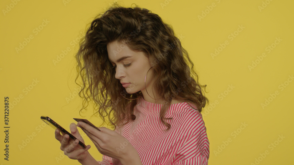 Young woman using money apps in smartphone for pay bank card in yellow studio Young woman using money apps in smartphone for pay bank card in yellow studio