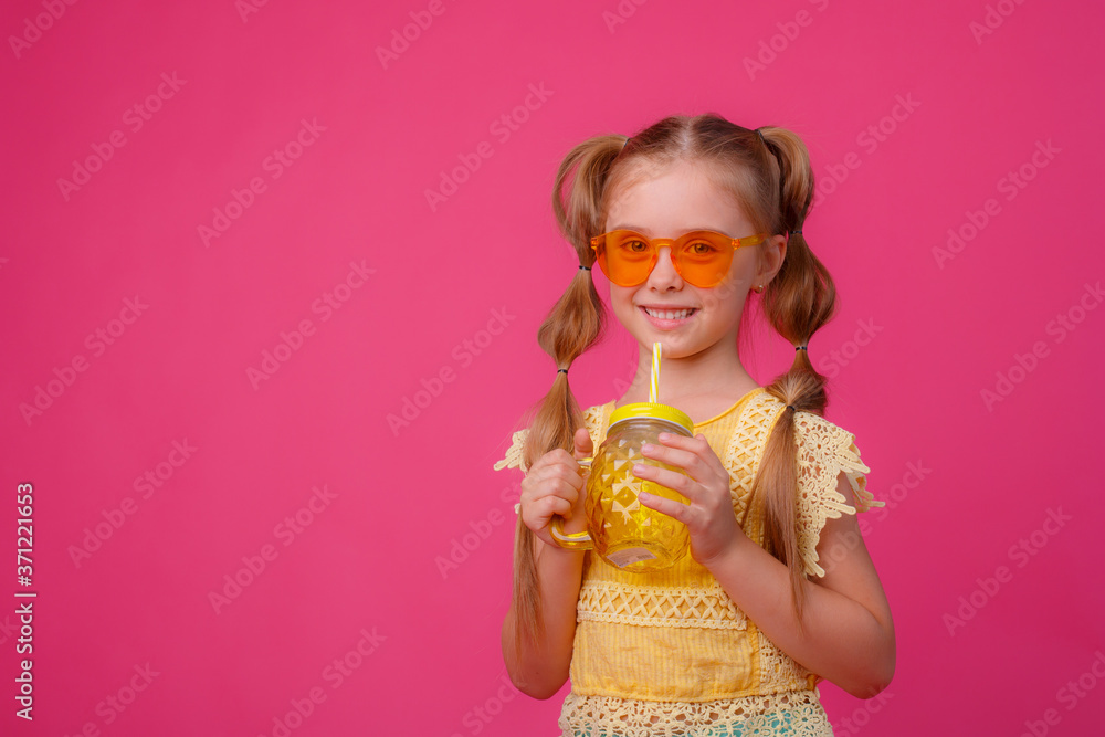 portrait of a little blonde girl in sunglasses on pink with a glass jar of cooling cocktail.