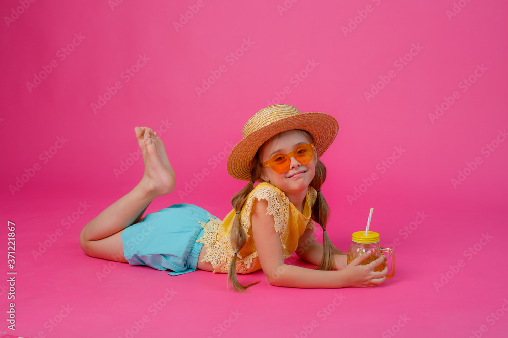 a little girl in sunglasses , a straw hat and a cocktail is lying on a pink background a little girl in sunglasses , a straw hat and a cocktail is lying on a pink background