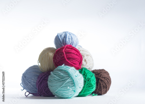 Stack of colorful yarn balls on a white surface and white background. Pile of knitting or crochet supplies, ready to be made into a warm clothing item.