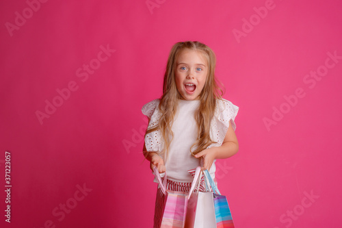 a little Girl with a lot of shopping bags on a pink background in the Studio, happy