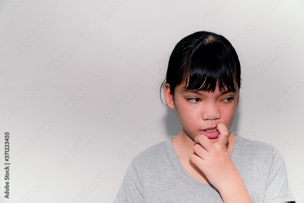 An Asian girl bites a nail and is stressed about something. The gray wall background, the problem of today's kids biting their nails, maybe due to personal problems or social misunderstandings. An Asian girl bites a nail and is stressed about something. The gray wall background, the problem of today's kids biting their nails, maybe due to personal problems or social misunderstandings.