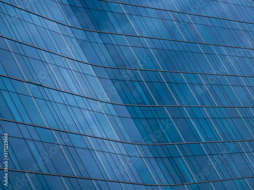 Abstract view of curved glass window panels on a commercial or corporate style building. Deep dark blue color on reflective diagonal surface.