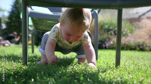 Curious blond baby collects small stones on the green grass of the meadow. Child on vacation in the summer. Childhood. Sunny day