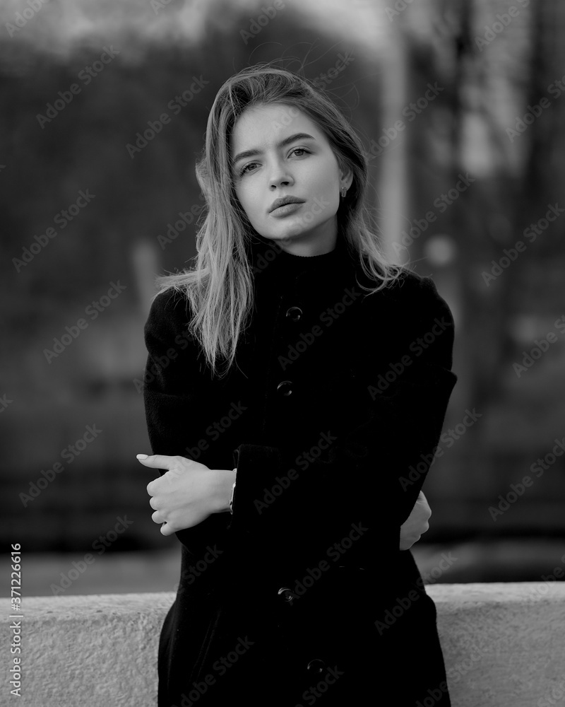 Young brunette woman at the black coat posing at the city