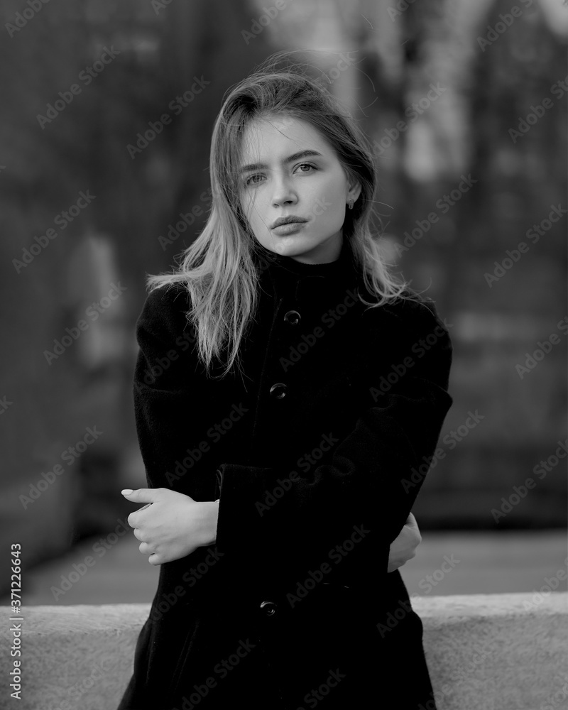 Young brunette woman at the black coat posing at the city