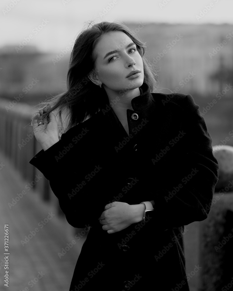 Young brunette woman at the black coat posing at the city