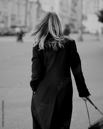 Young brunette woman at the black coat posing at the city