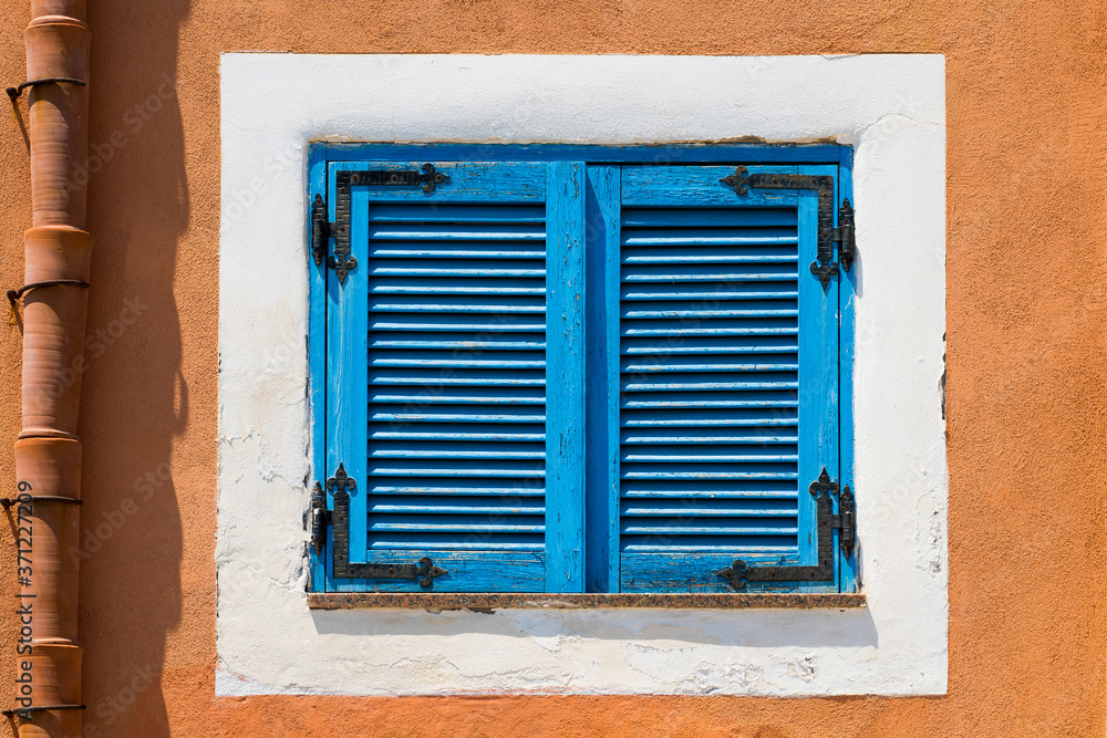 Blue wooden window on a white and orange wall, colorful houses in Salina, typical building of the Aeolian Islands, Sicily, Italy.