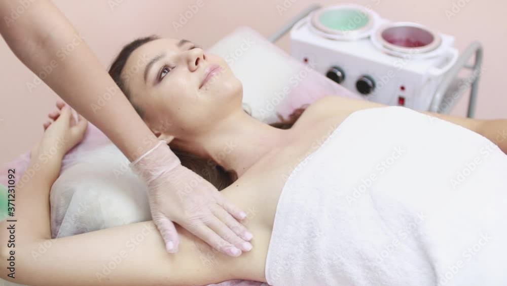 The master removes unwanted hair from the armpit area of a young woman using wax. Sugaring. Depilation. Epilation. Beauty Concept. Selective focus. The master removes unwanted hair from the armpit area of a young woman using wax. Sugaring. Depilation. Epilation. Beauty Concept. Selective focus.