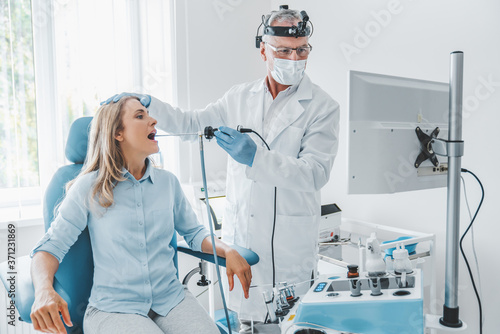 Senior otolaryngologist making endoscopic examination while looking in monitor for female patient at office photo