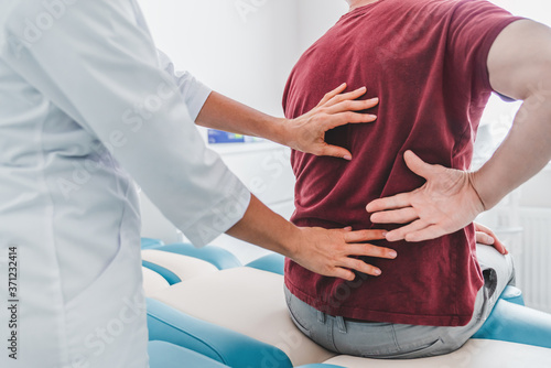 Cropped close up of female orthopedist examining patient's back in clinic photo